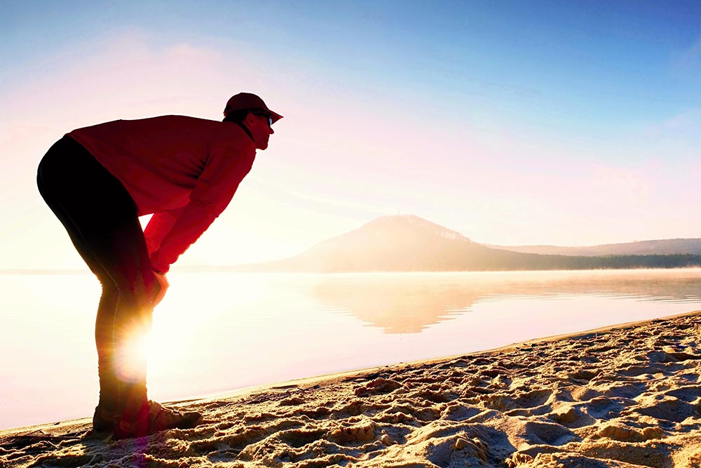 anaheimlighthouse-7-tips-for-staying-sober-while-traveling-article-photo-man-doing-breathing-exercises-beach-silhouette-of-active-man-exercising-and-stretching-on-the-lake-beach-616755629