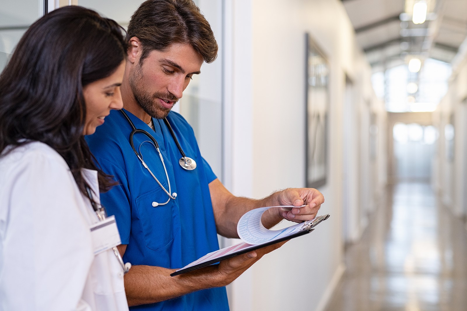 Team of doctors working together on patients file at hospital. Medical staff analyzing report and working at clinic. Woman doctor having discussion in a hospital hallway with nurse, copy space.