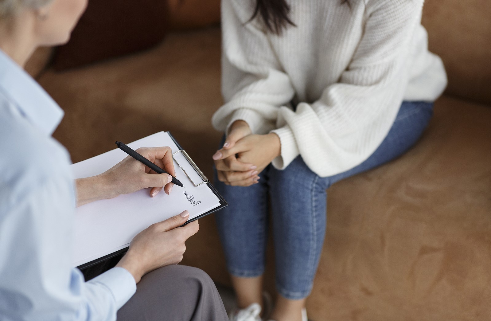 Unrecognizable Psychologist Talking With Female Client Taking Notes During Psychotherapy Session Sitting In Office. Selective Focus, Cropped