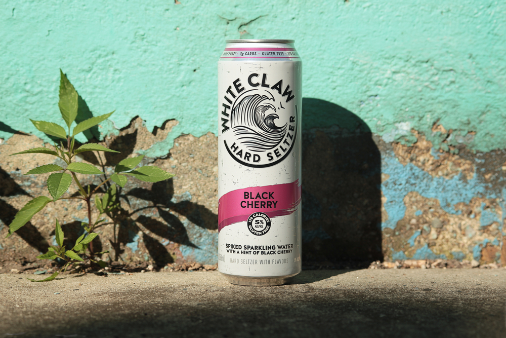 White Claw Original Blackberry flavor on a concrete surface and green wall