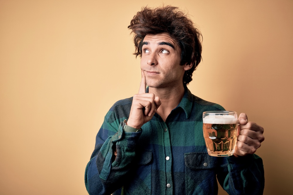 Man with a questioning face holding a mug of beer