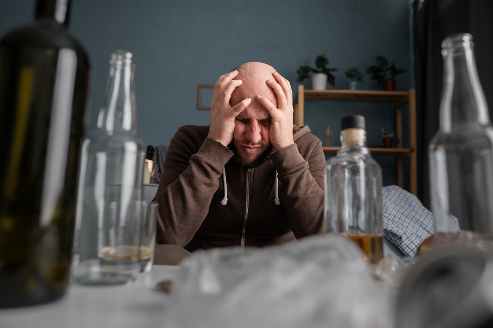Anxious man with hands on his face with several bottles of alcohol on the table